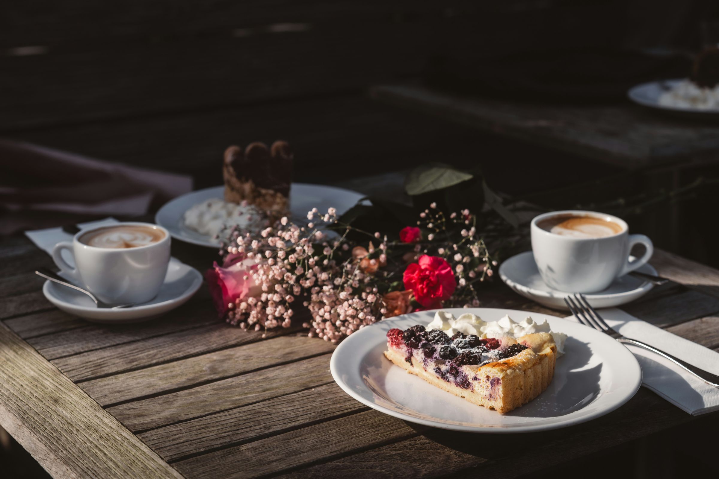 Zwei Tassen Kaffee und ein Stück Beerenkuchen auf einem Holztisch im Morgenlicht