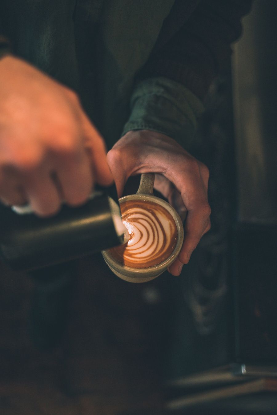 Hände giessen Milchschaum in eine Tasse Kaffee